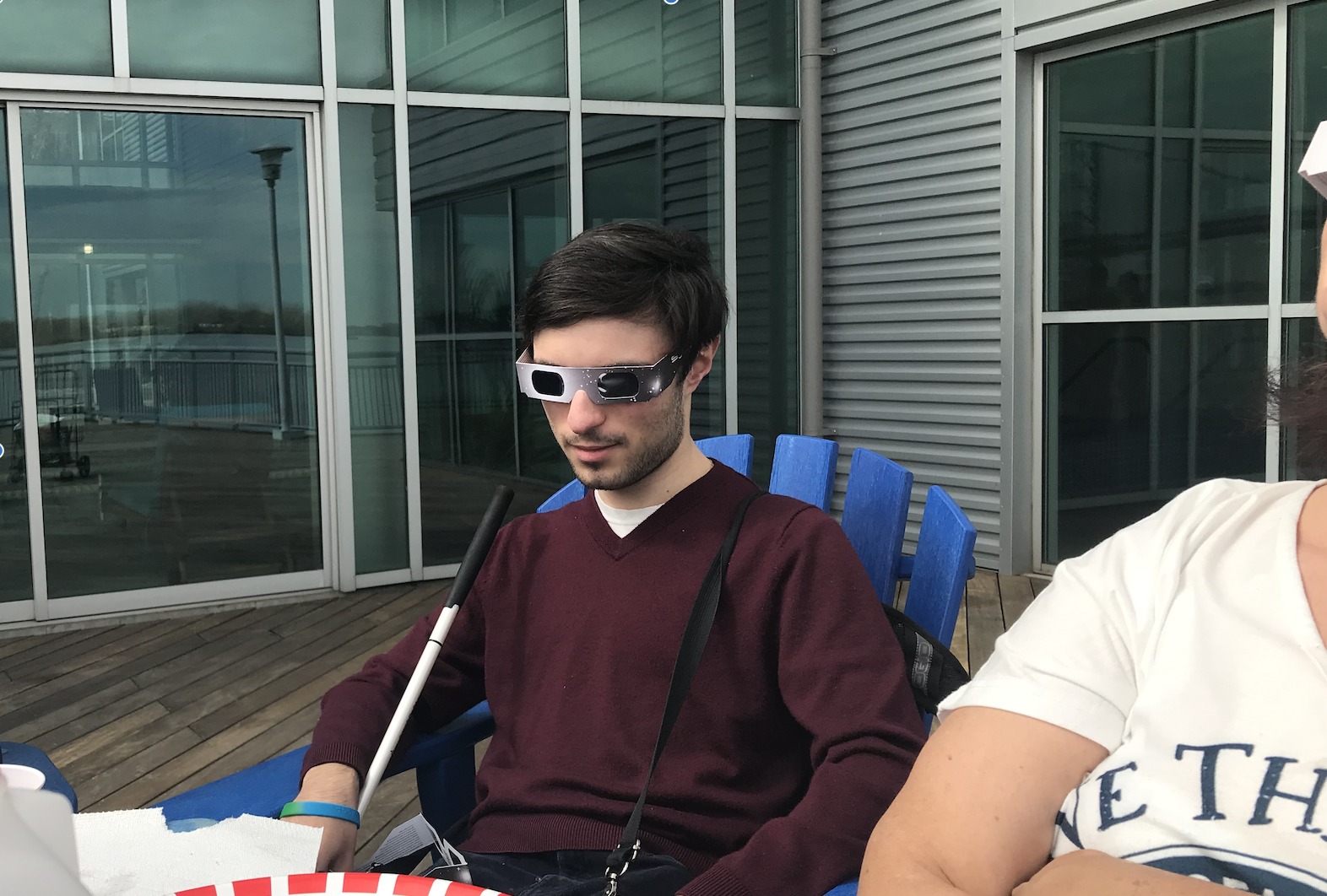 A person in a maroon sweater on a blue chair sits outside during the 2024 solar eclipse in philadelphia, using LightSound to experience the event